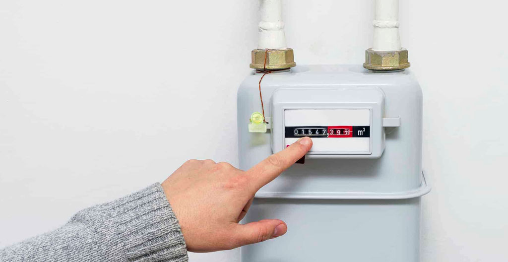 Un compteur de gaz industriel dans un local technique d'immeuble, légèrement poussiéreux, éclairé par une lumière naturelle faible